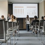 Business conference attendees listen to a presentation on revenue split by quarter and geography.